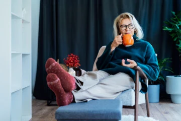 middle aged woman relaxing with pumpkin shaped cup of hot drink in scandy style hygge interior home with fall mood decor. lady dreaming, enjoy calm mood without stress, well being alone. cozy autumn.